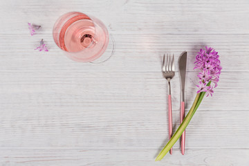 Pink rustic table setting with purple hyacinth flowers, linen napkin and glass of rose wine on white wooden table