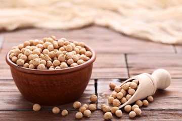 Chickpeas in bowl and scoop on brown wooden table