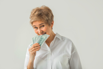 adult stylish woman in white shirt on a white background bites dollars