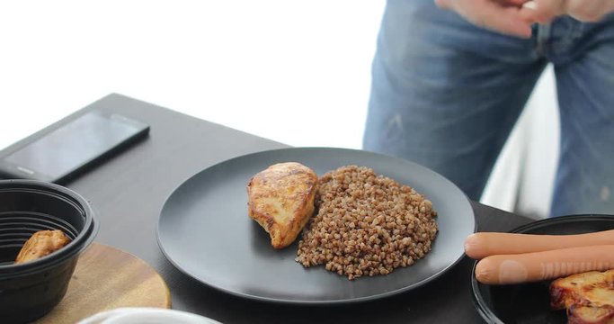 Man takes piece of meat and puts plate next to buckwheat. Home cooking dinner