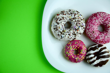 Assorted donuts with chocolate frosted, pink glazed and sprinkles donuts. Green pastel background. Copy space for text. Horizontal.