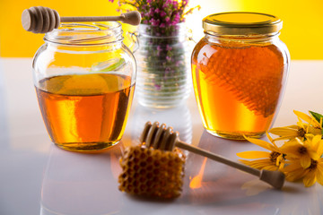 Honey dripping from a wooden honey dipper in a jar on wooden background
