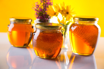 Honey dripping from a wooden honey dipper in a jar on wooden background