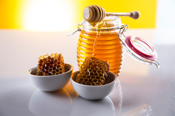 Honey dripping from a wooden honey dipper in a jar on wooden background