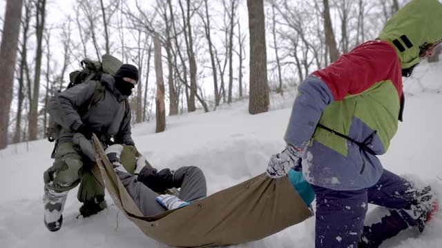 hikers are carrying woman with broken leg on palanquin in forest, stepping over snowdrifts