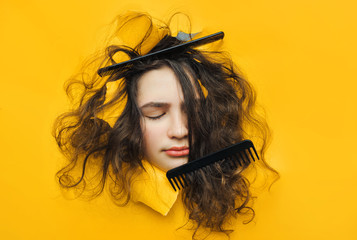 A funny teenage sad girl with problematic curly hair expresses displeasure on her face. Two combs tangled in hard hair.