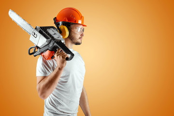 Bearded man in a helmet holds a chainsaw on an orange background. Construction concept, contractor,...