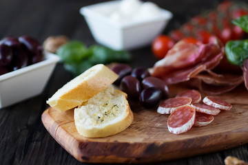 Prosciutto, bread, olives, walnut, mozzarella, salami, basil and cherry tomatoes on  brown wooden board.  Mediterranean kitchen.