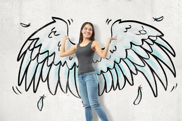 Young brunette girl wearing casual jeans and t-shirt with cartoon wings drawn on white wall...