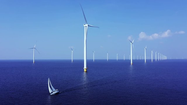 WindTurbines in a blue sea on a sunny day with a sailing boat passing by.