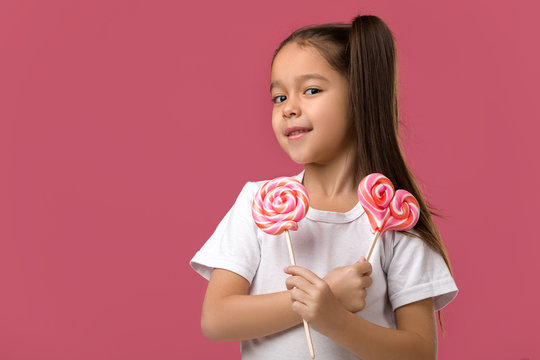 Beautiful smiling little child girl with sweet candy lollipop isolated on pink background