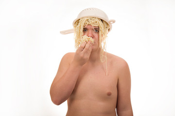 A young, fat, cheerful, smiling boy eating pasta and having a colander and spaghetti on his head. Plump body without clothing. White background. Portrait photo.