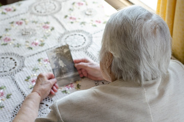 Older woman looking to the photo with young herself. Old photos, nostalgie