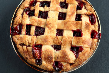 Traditional delicious cherry pie with a lattice of dough on a black graphite background with free space for text.  Holiday treat