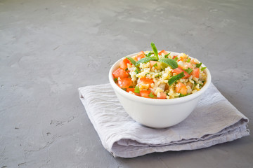 Tabbouleh salad with bulgur, parsley, mint  and tomato in a white bowl on a gray concrete background with copy space for text. Traditional Lebanese Arabic Salad