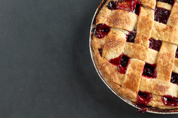 Traditional delicious cherry pie with a lattice of dough on a black graphite background with free space for text.  Holiday treat