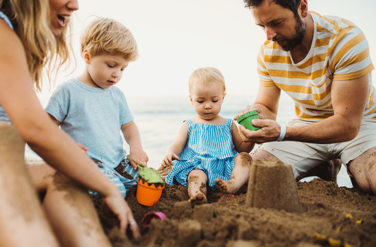 Young family with toddler children playing with sand on beach on summer holiday.