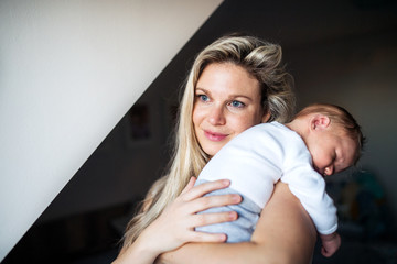A beautiful young mother with a sleeping newborn baby at home. Copy space.