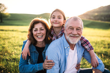 Senior couple with granddaughter outside in spring nature, relaxing on the grass.