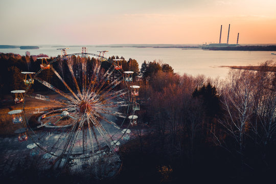 Old abandoned ferris wheel carousel in front of power plant chimneys. This abandoned park is in Elektrenai city in Lithuania, but feels like being in Chernobyl. Drone photo.