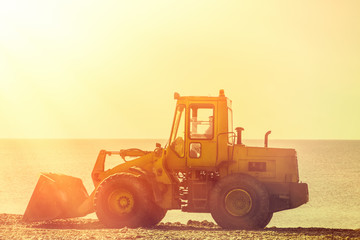 Bulldozer rides on the beach. In the background sea and sky. Tint and light