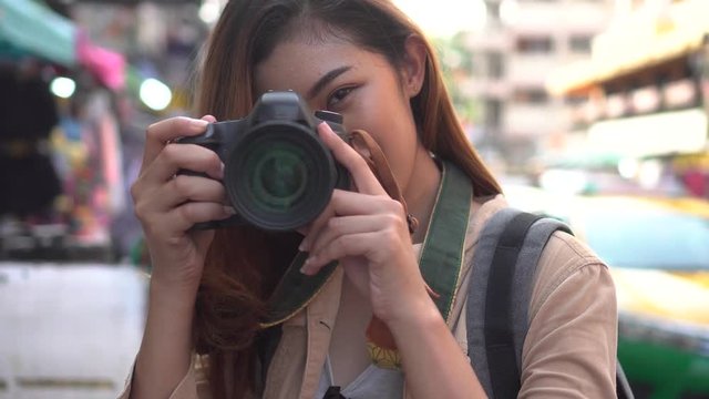 Young Asian female tourist woman with smile holding a camera and taking photos in Bangkok, Thailand while travelling in Southeast Asia
