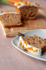 Loaf of carrot cake with cream cheese frosting and candy garnish on wooden table