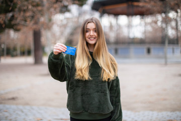 Happy young lady with credit card while standing in park