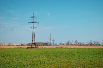 Green field and blue sky, in the distance power lines with many wires.