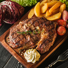 Ribeye steak with potatoes, onions and baked cherry tomatoes. Juicy steak with flavored butter
