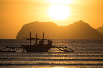 Boat silhouette on sunset and isles background. Traditional Philippines fishing boat at sunset. Boat in the sea. Golden sunset above the sea. Travel and transportation concept. Sailboat on seascape.