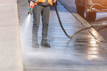 Worker cleaning driveway with gasoline high pressure washer splashing the dirt, granite embankment. High pressure cleaning.