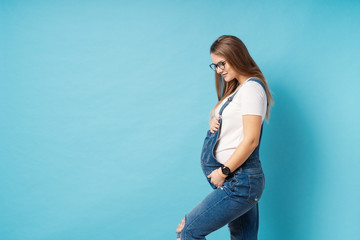 Smiling pregnant woman wearing glasses caressing her belly over blue background