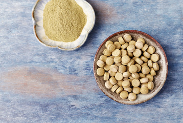 Bio Green BARLEY GRASS tablets and powder. Concept for a healthy dietary supplementation. Rustic wooden background. Top view. Copy space. 