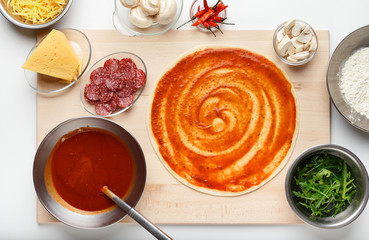 Raw dough for pizza preparation with ingredient in bowls