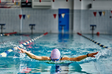 Female athlete swims with a butterfly style. Splashes of water scatter in different directions.