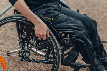 Naklejka premium Close-up of male hand on wheel of wheelchair during walk in park