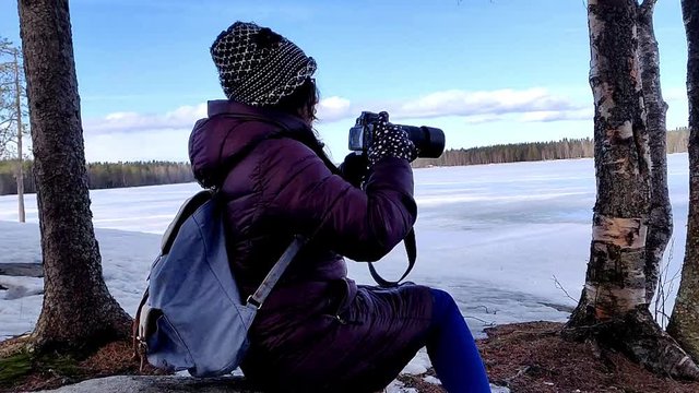 Beautiful winter woman taking pictures in the woods of snow covered nature in a cold windy day in slow motion