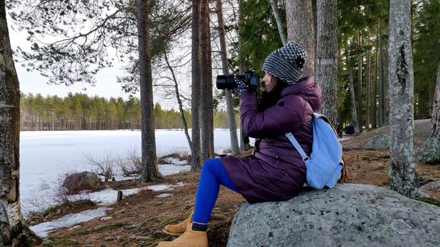 Thoughtful beautiful woman taking pictures in the woods of snow covered nature in a cold windy day in slow motion