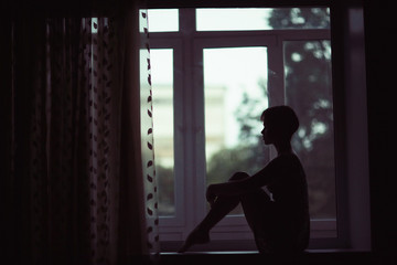 Silhouette of sad girl sitting on window