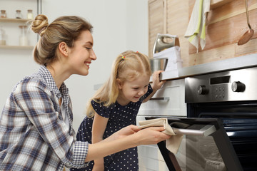 Mother and her daughter baking food in oven at home