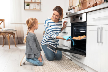 Mother and her daughter taking out cookies from oven in kitchen