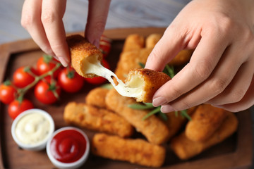 Woman holding broken cheese stick over board, closeup