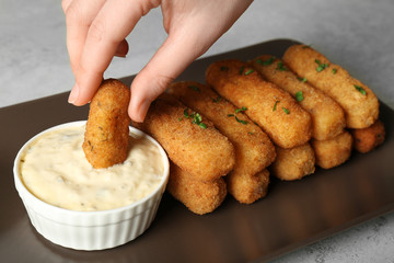 Woman dipping cheese stick into sauce at table, closeup