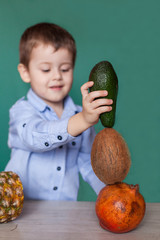 Fototapeta premium Cute little boy with exotic fruits on green background. Selective Focus of Fruit