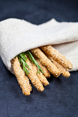 Italian grissini or salted bread sticks with rosemary herb on linen napkin on black board background.