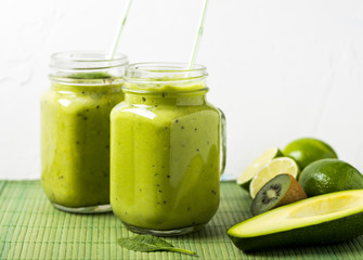 Green smoothie made by avocado, lemon and kiwi on green background.