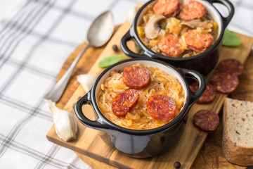 Slovak Christmas national cabbage soup in small black pot with sausage on the tablecloth background.