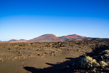 Spain, Lanzarote, Red volcano mountains of timanfaya national park behind endless black lava field