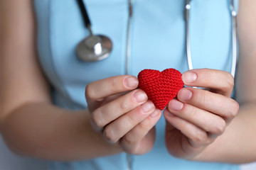 Cardiology and health care, woman doctor holding red knitted heart in hands. Concept of...